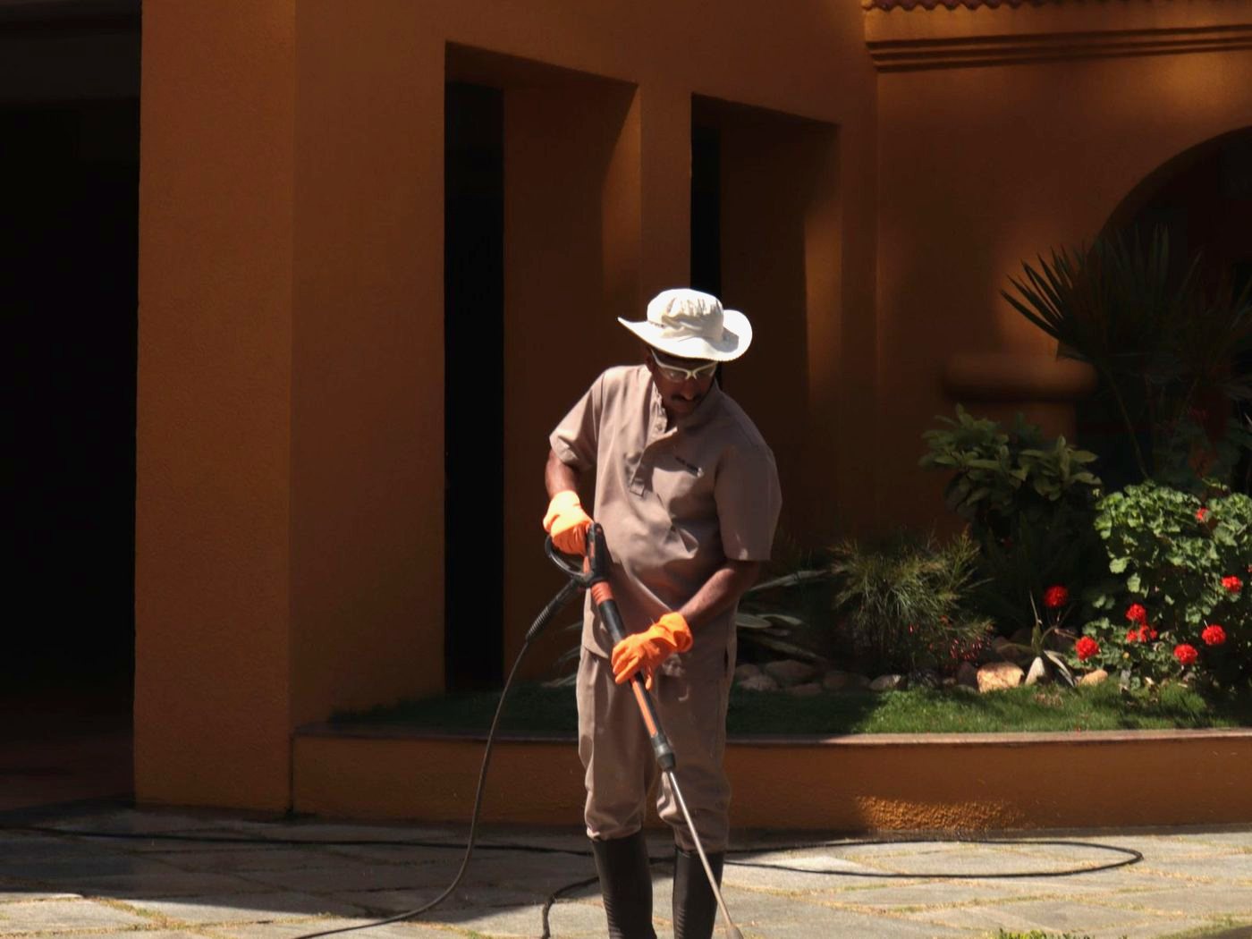 Pressure washing a paved walkway beside a stucco wall in strong afternoon sun